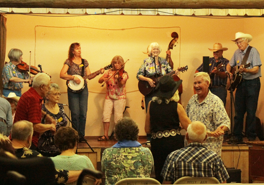 OOTFA members playing fiddle, banjo, guitar and bass while audience members dance at a community hall jam session